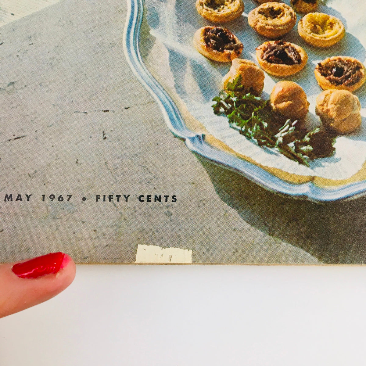Close-up of the Gourmet Magazine of Good Living May 1967 showing a plate of fine hors d'oeuvres with a finger pointing to the magazine details.