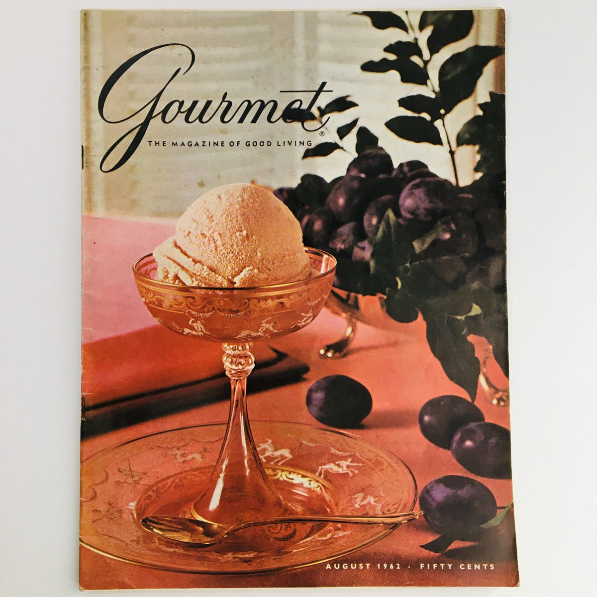 Cover of Gourmet Magazine of Good Living from August 1962 featuring a scoop of ice cream in an elegant glass, surrounded by fresh fruits, highlighting the issue's theme 'The Cordial Touch'.