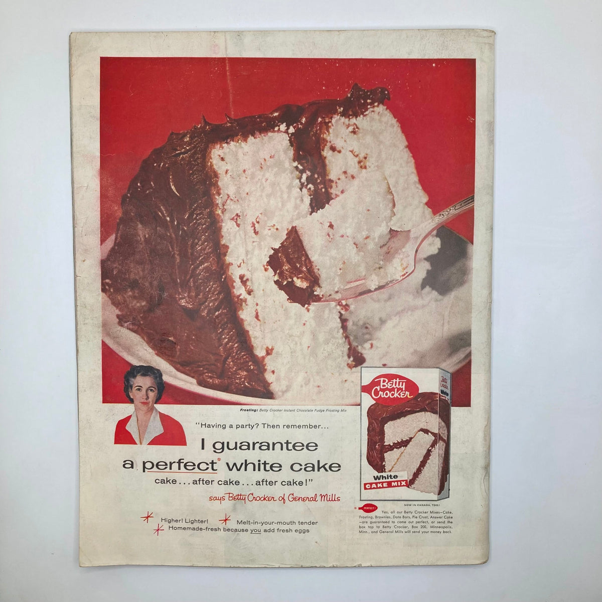 Vintage advertisement for Betty Crocker White Cake Mix featuring a photo of a deliciously layered cake with chocolate frosting on a red background, promoting the perfect cake for parties.