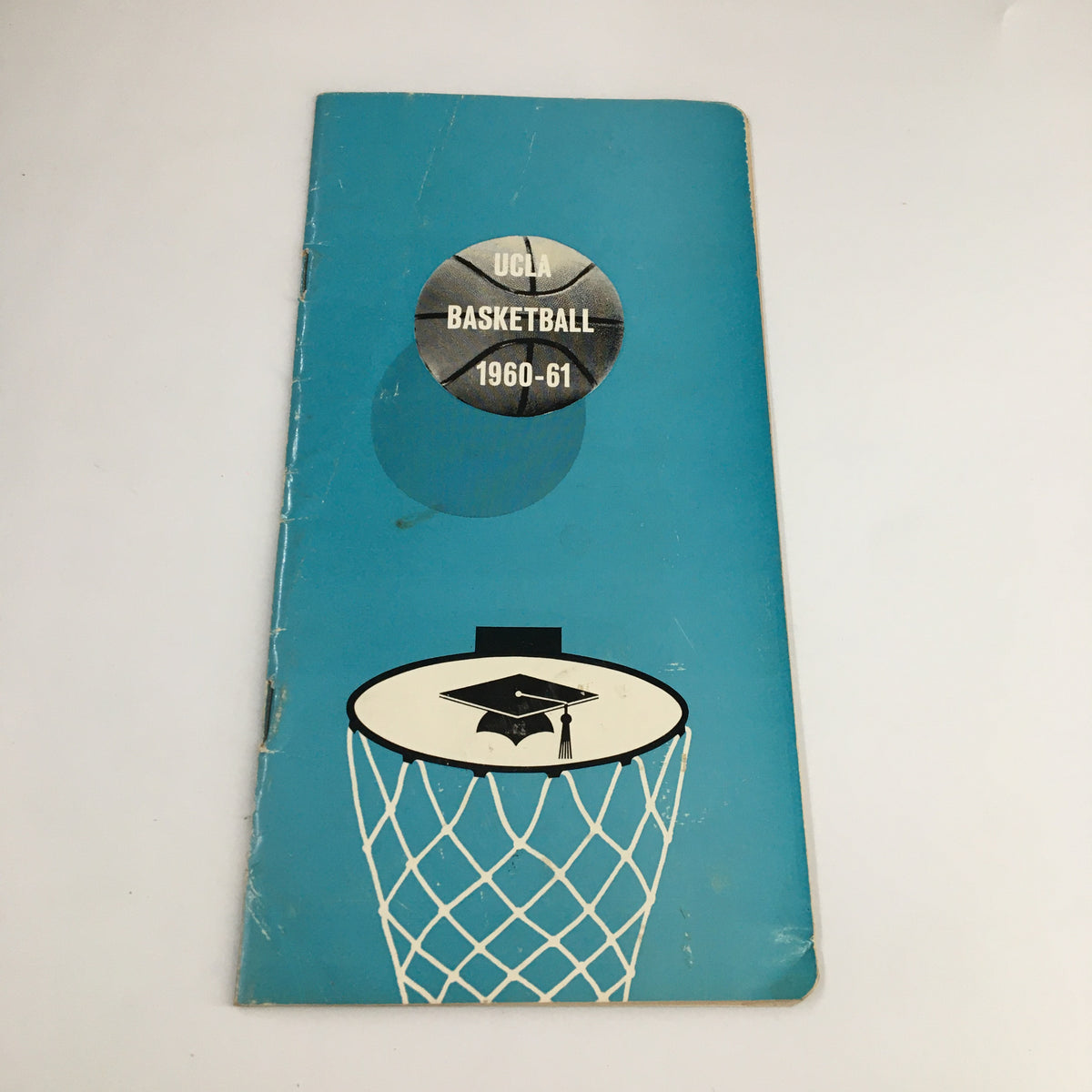 1960-1961 NCAA UCLA Bruins Varsity Basketball Schedule Program cover featuring a blue design with a basketball graphic and a graduation cap on a hoop.