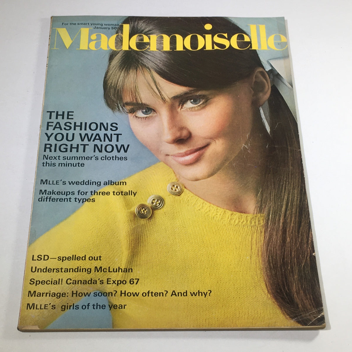 VTG Mademoiselle Magazine from January 1967 featuring the cover with a young model in a stylish yellow sweater, showcasing fashion trends of the era. The cover highlights various topics including wedding albums, make-up tips, and marriage advice.