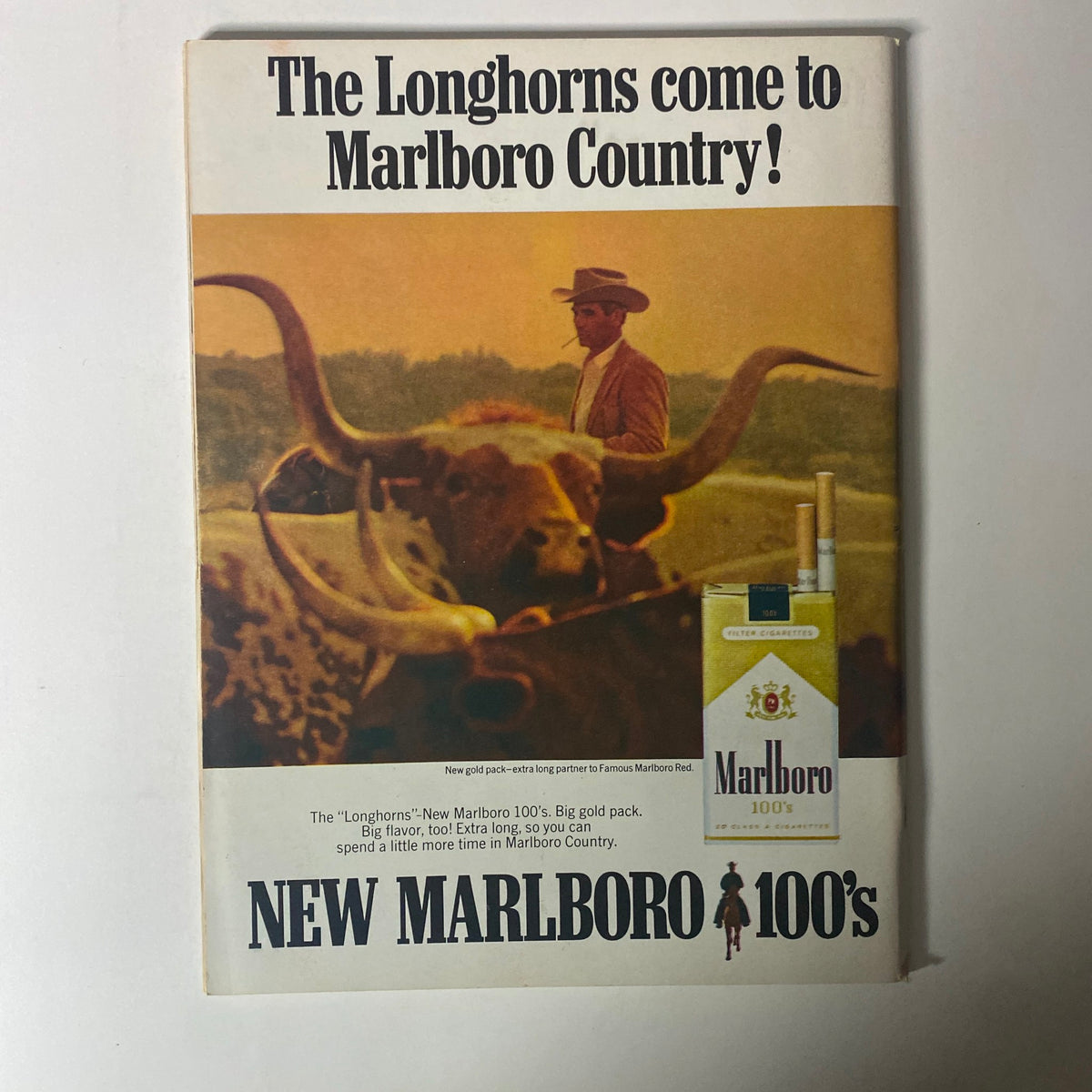 Advertisement for New Marlboro 100's cigarettes, showcasing a cowboy and longhorn cattle with a scenic background. This image captures the essence of the Marlboro Country theme.