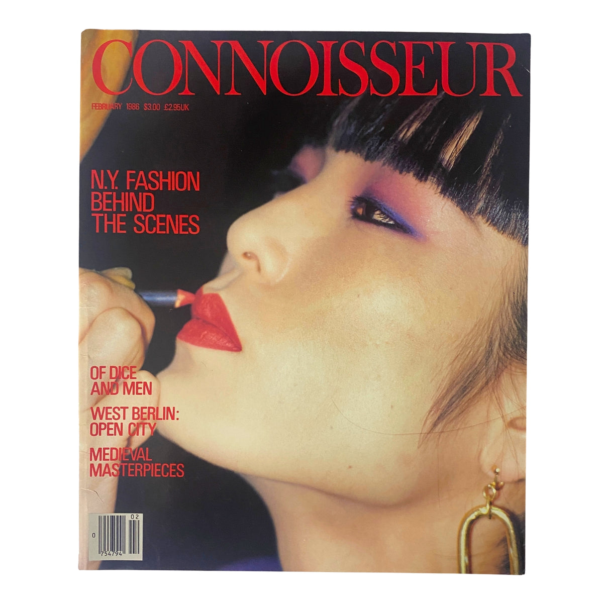 Cover of Connoisseur Magazine February 1986 showcasing N.Y. Fashion Behind The Scenes with a model applying lipstick, featuring bold makeup and earrings.
