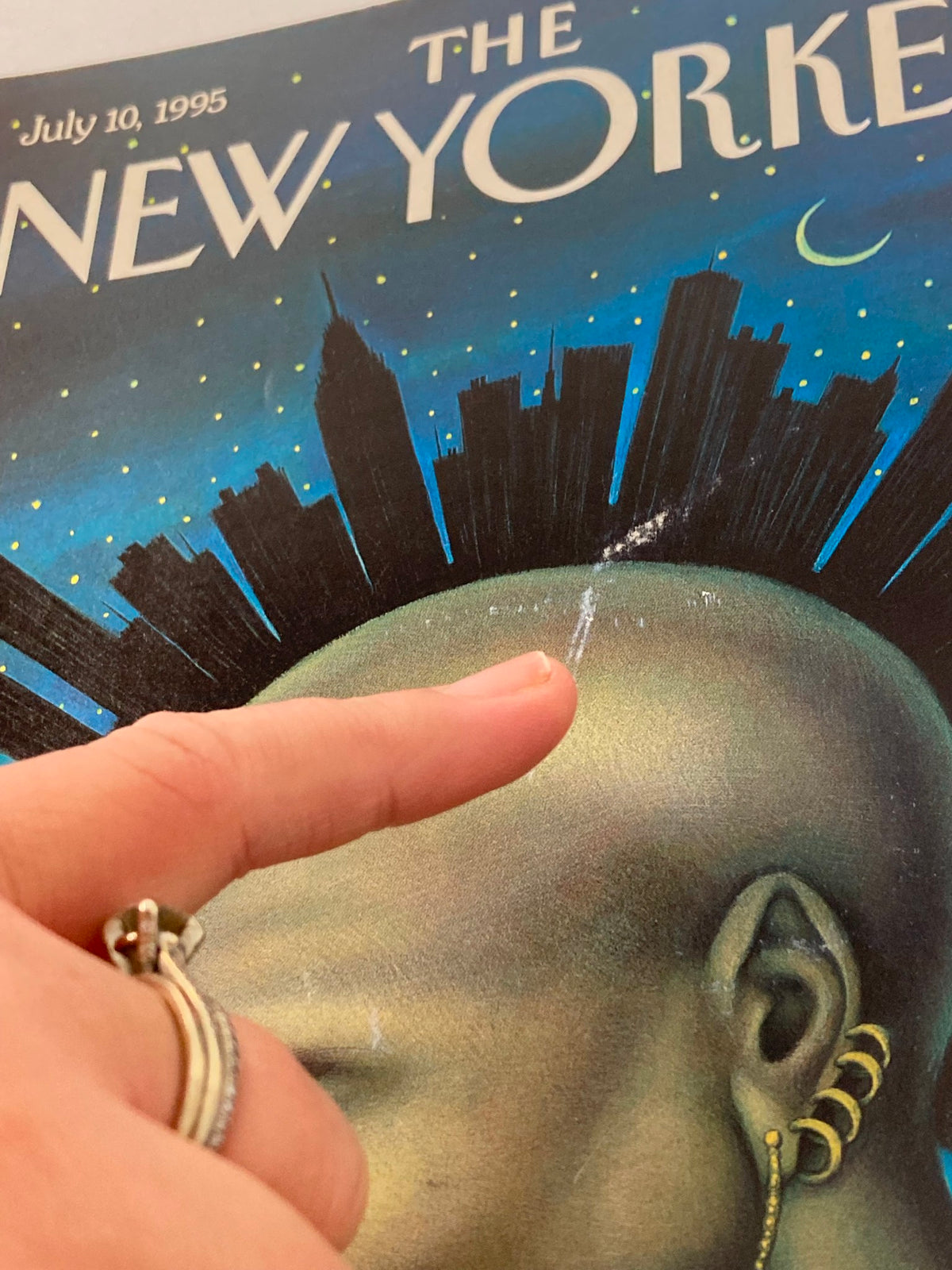 Detail shot of The New Yorker cover dated July 10, 1995, featuring the artwork 'Mohawk Manhattan' by Anita Kunz, with a finger pointing at minor imperfections on the cover.