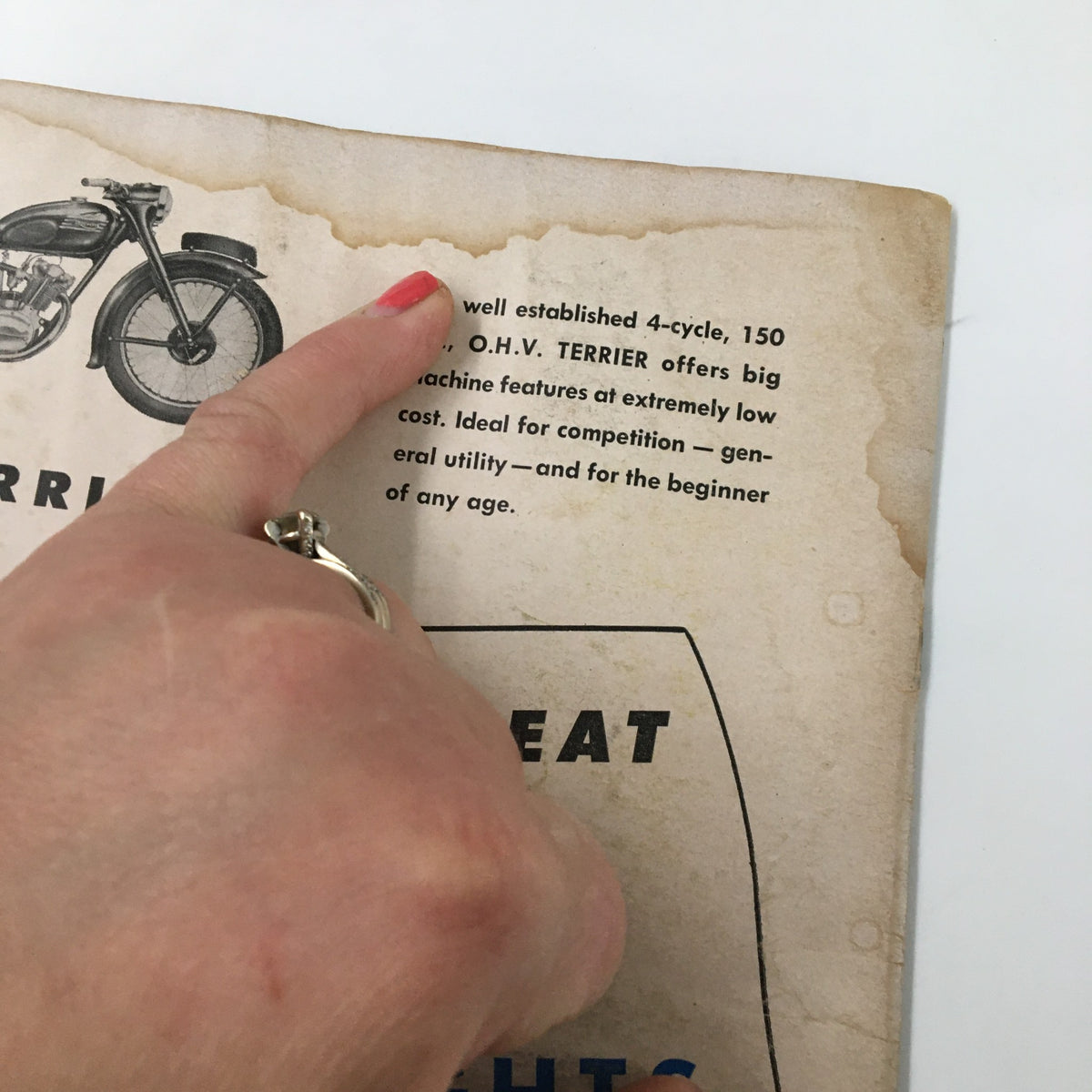 Close-up image showing a hand pointing at a vintage advertisement in the VTG Cycle Magazine July 1954, featuring a road test for The 'Catalina' Velo.