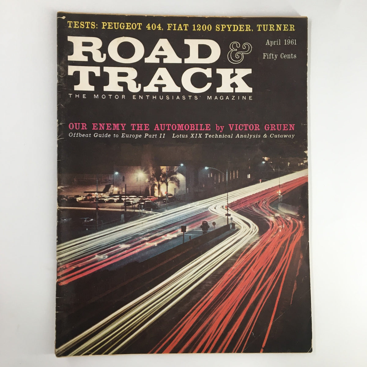 VTG Road & Track Magazine April 1961 cover featuring the title 'Our Enemy The Automobile' by Victor Gruen. The magazine showcases a night scene of illuminated car lights in motion, representing the automotive culture of the early 1960s.