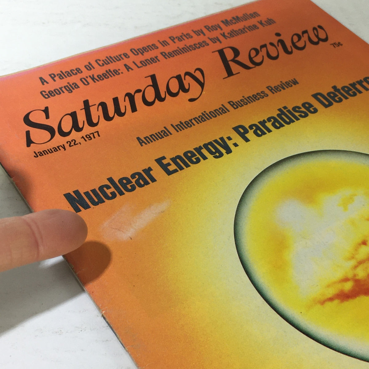 Close-up of the VTG Saturday Review: January 22 1977 cover by Katherine Kuh, showing the magazine title and the headline 'Nuclear Energy: Paradise Deferred,' with a finger pointing at the cover highlighting minor imperfections.