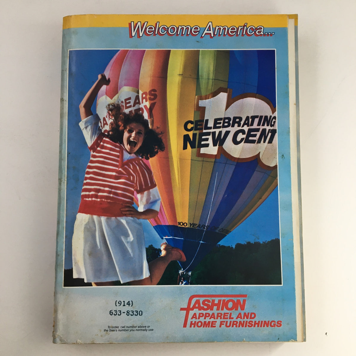 VTG 1986 Centennial Edition Fashion Apparel & Home Furnishing Catalog cover featuring a woman in a striped shirt celebrating under a colorful hot air balloon.