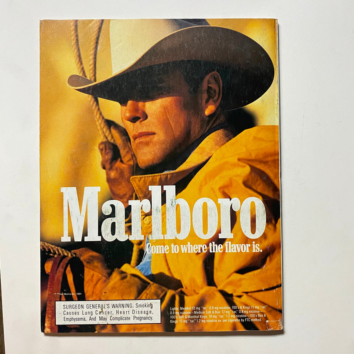 Back cover of a Marlboro advertisement showcasing a cowboy in a yellow jacket with the slogan 'Come to where the flavor is' along with a health warning regarding smoking.