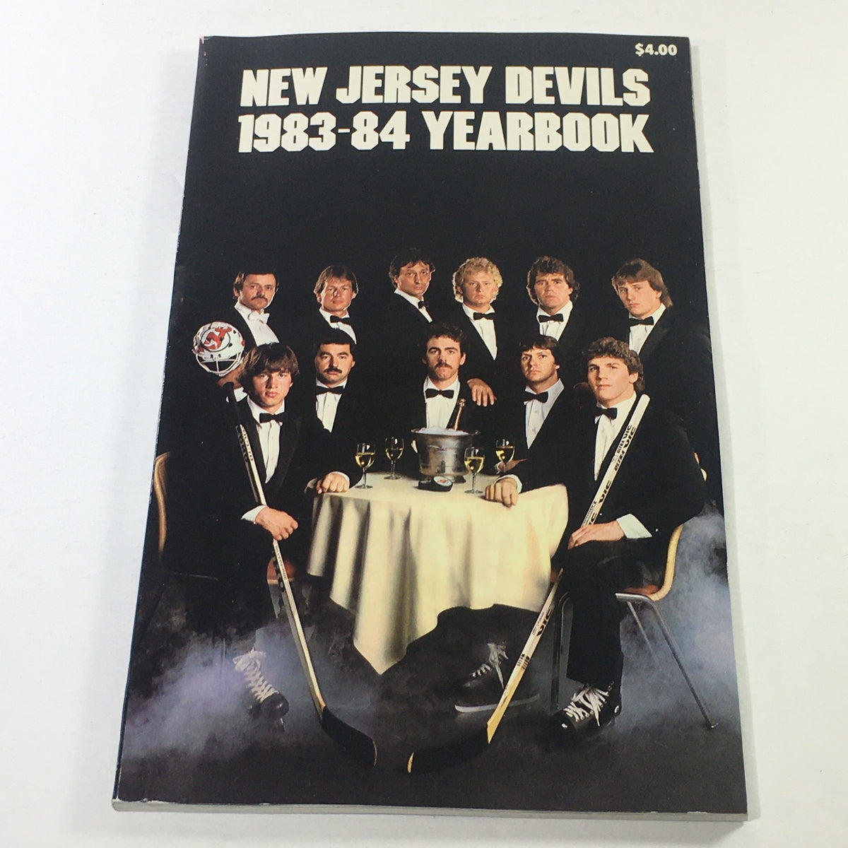 VTG NHL Official Yearbook 1983-1984 featuring the New Jersey Devils team photo with players dressed in tuxedos, gathered around a table with a trophy and glasses.