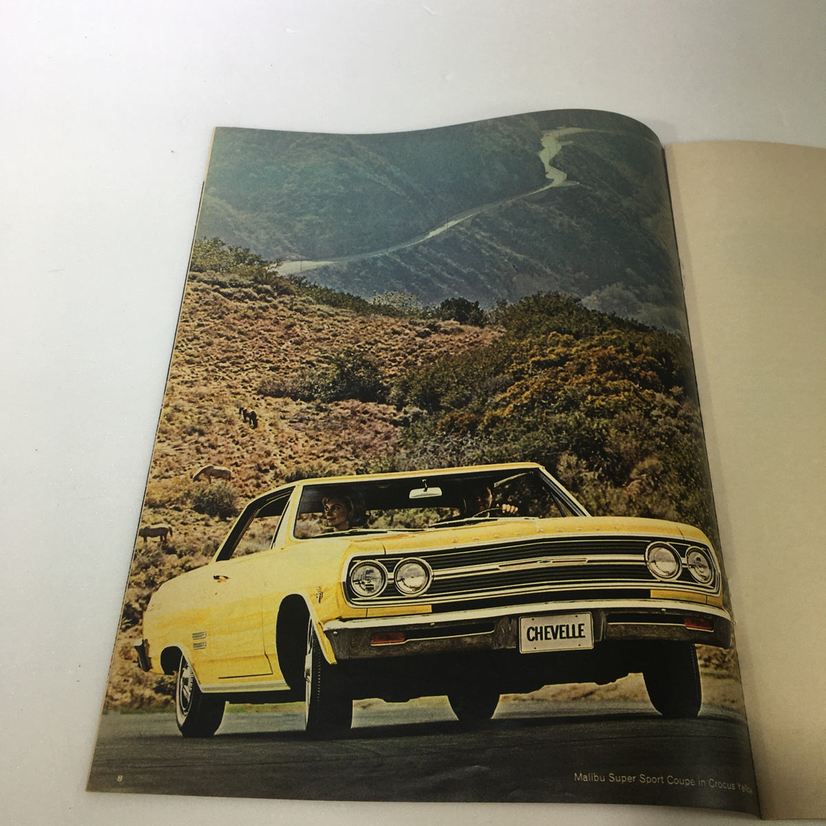Interior page of the VTG 1965 Chevrolet Chevelle Corvair Chevy II Corvette Car Auto Brochure Catalog showing a yellow Malibu Super Sport Coupe driving through a scenic mountainous landscape.