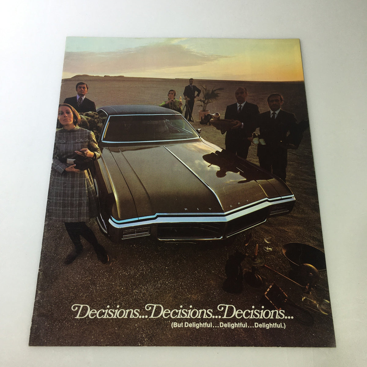 Vintage 1969 Buick Motor Division Electra 225 car auto brochure catalog featuring a stunning image of a dark-colored Buick Riviera parked on a sandy landscape with six individuals elegantly dressed, highlighting the theme 'Decisions...Decisions...Decisions...' in an illustrative 1970s advertising style.