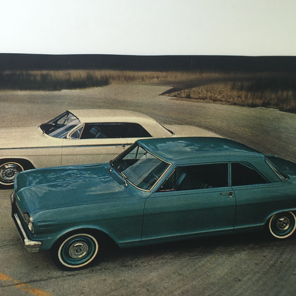 A vintage scene featuring classic cars from the 1962 era, including a blue vehicle and a white convertible, featured in the VTG 1962 Complete Magazine Guide To New Cars.