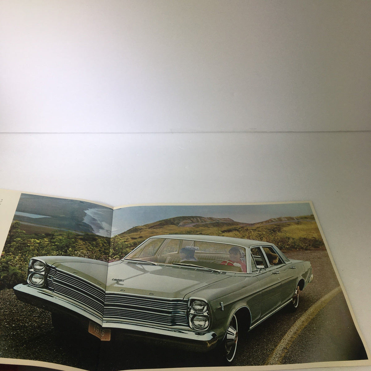 Interior view of the VTG 1966 Ford Galaxie 500 Convertible Sedan brochure, featuring a light green car parked on a scenic road with passengers inside.