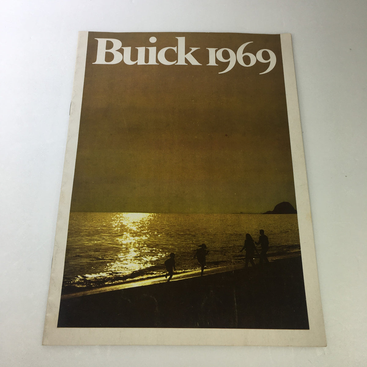Cover of the VTG 1969 Buick Riviera GS Electra Custom Sport Coupe Car Auto Brochure Catalog featuring a serene beach scene with silhouettes of people walking along the shore during sunset.