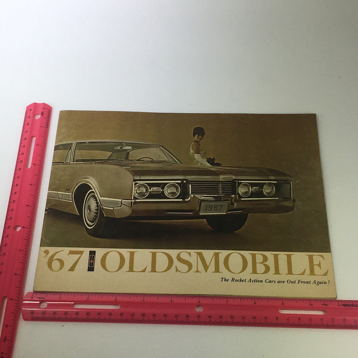 Front view of the VTG 1967 Oldsmobile Toronado Delta Sedan Car Auto Brochure Catalog with a classic car and a model, showcasing the retro design.