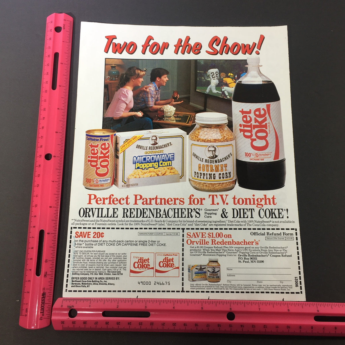 Close-up view of the vintage 1985 Coca-Cola Diet Coke and Orville Redenbacher's Popcorn ad coupon with a ruler for size reference, emphasizing the promotional offers and joyful TV viewing.