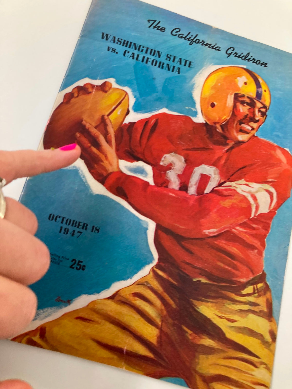 Close-up of the October 18, 1947 Football Official Program cover showcasing the Washington State vs. California match, with a hand pointing at the player illustration.