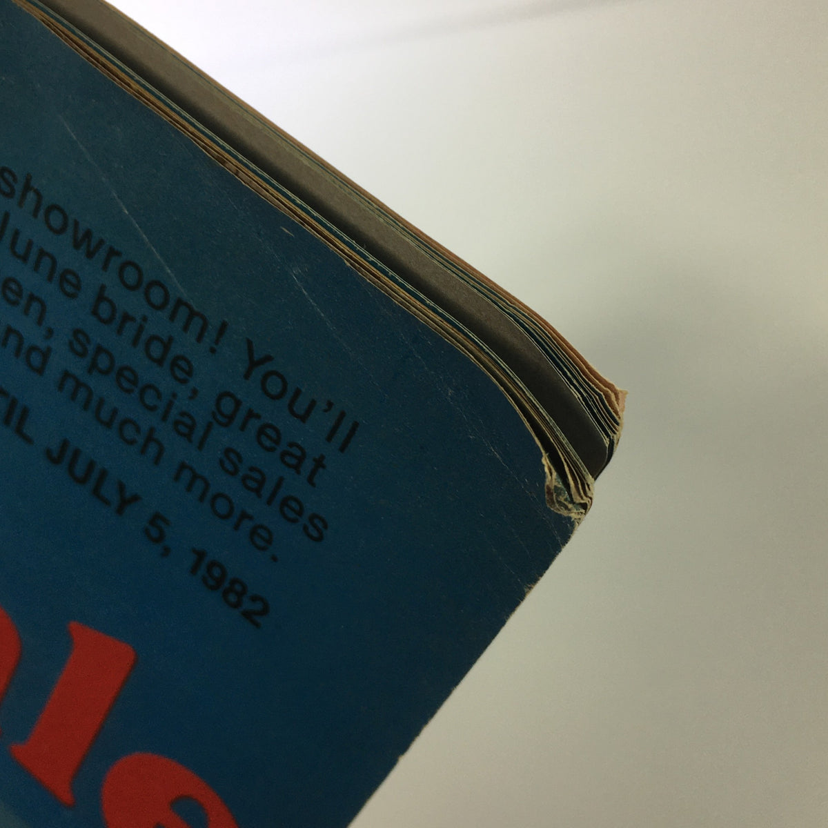 Close-up of the worn edge of the VTG 1982 Service Merchandise Catalog Showroom Summer Home Furniture Sale Guide, showing binding wear and a vintage design.
