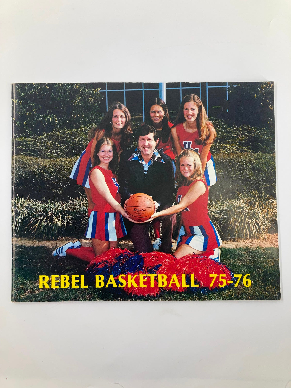 1975-1976 Rebel Basketball University of Mississippi Basketball Guide cover featuring cheerleaders and the basketball team.
