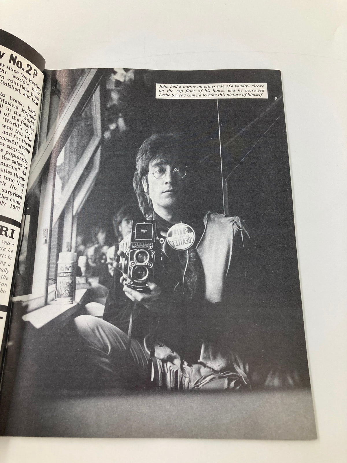 John Lennon captured in a reflective moment holding a camera, featured in The Beatles Book Monthly Magazine December 1986 #128, highlighting his artistic side and contribution to music history.
