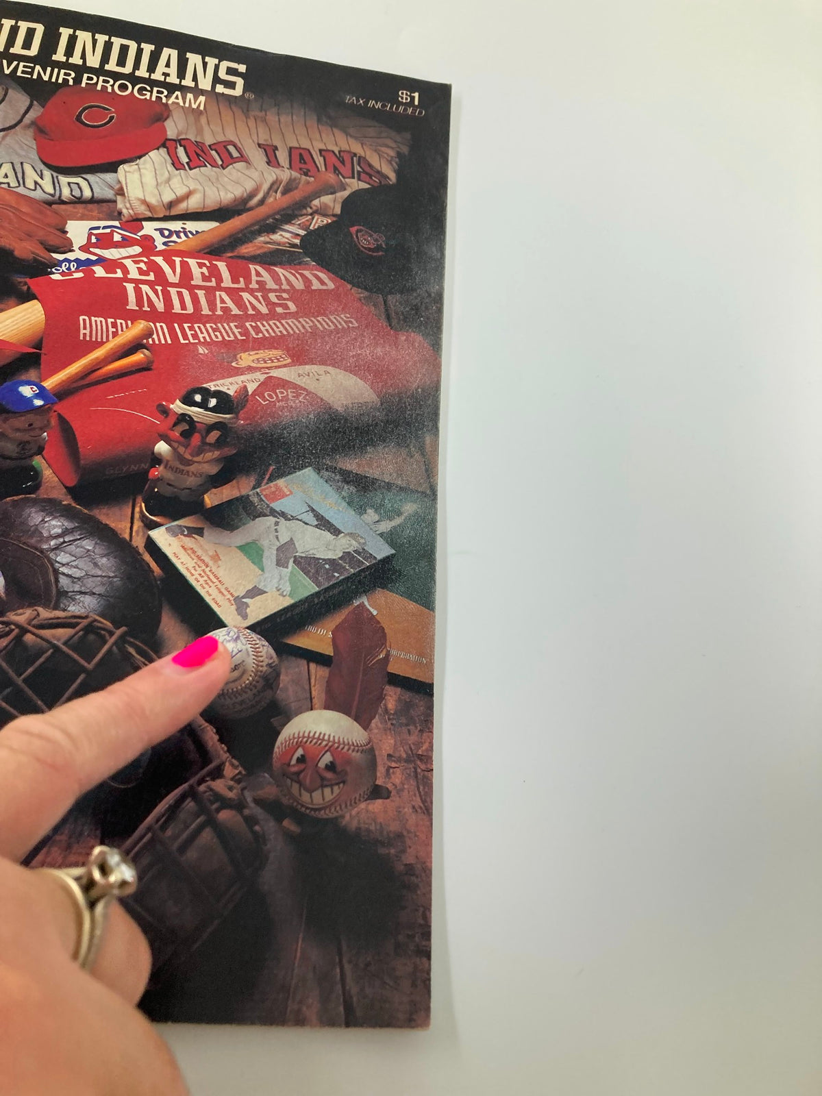 Close-up of the 1983 MLB Cleveland Indians Official Souvenir Program showing a hand pointing at baseball collectibles and memorabilia.