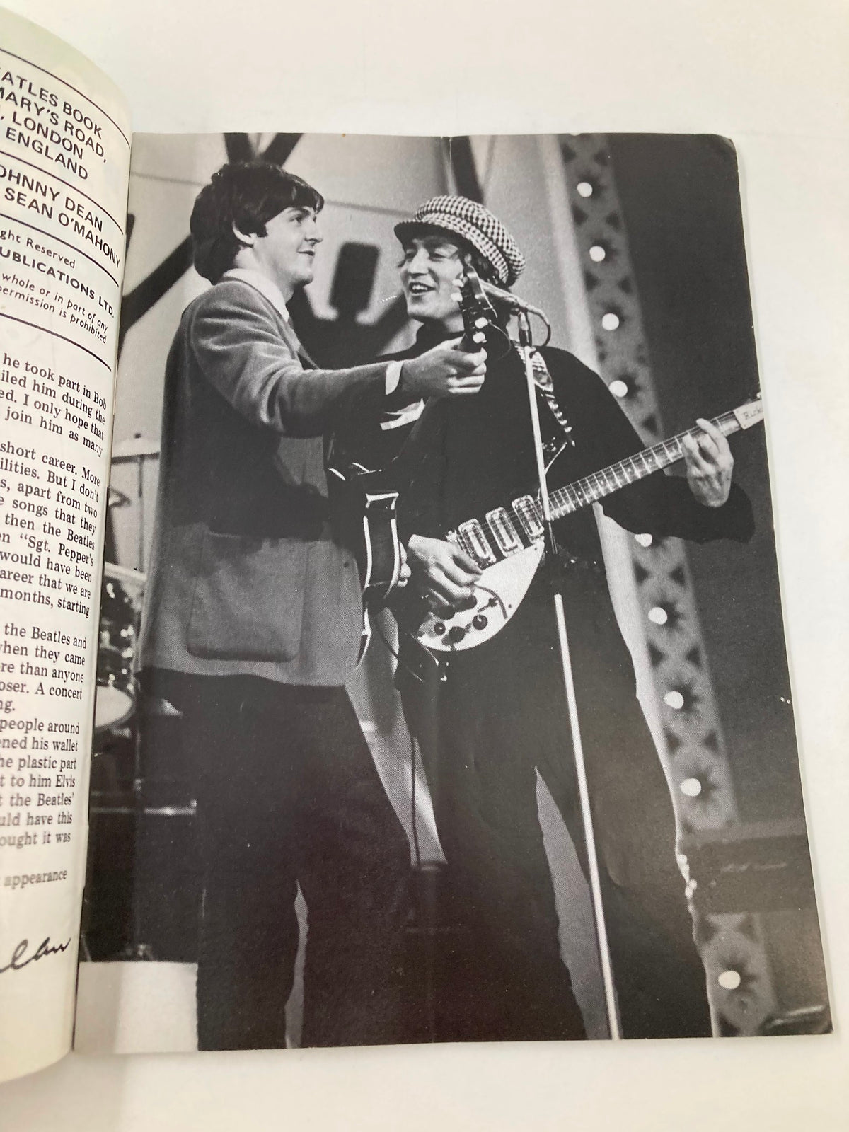 Black and white photo of Paul McCartney and John Lennon smiling together during a performance, featured in The Beatles Book Monthly Magazine September 1985 Issue #113.