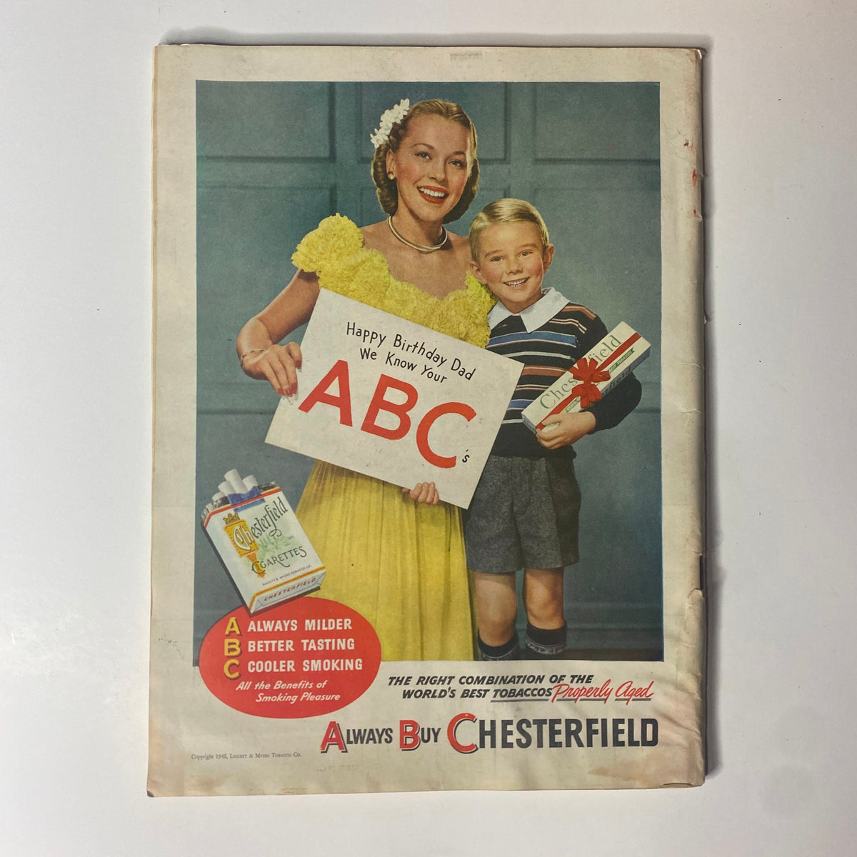 Vintage advertisement from a magazine featuring a smiling woman in a yellow dress and a boy holding a birthday sign. The ad promotes Chesterfield cigarettes with the tagline 'Always Buy Chesterfield.'