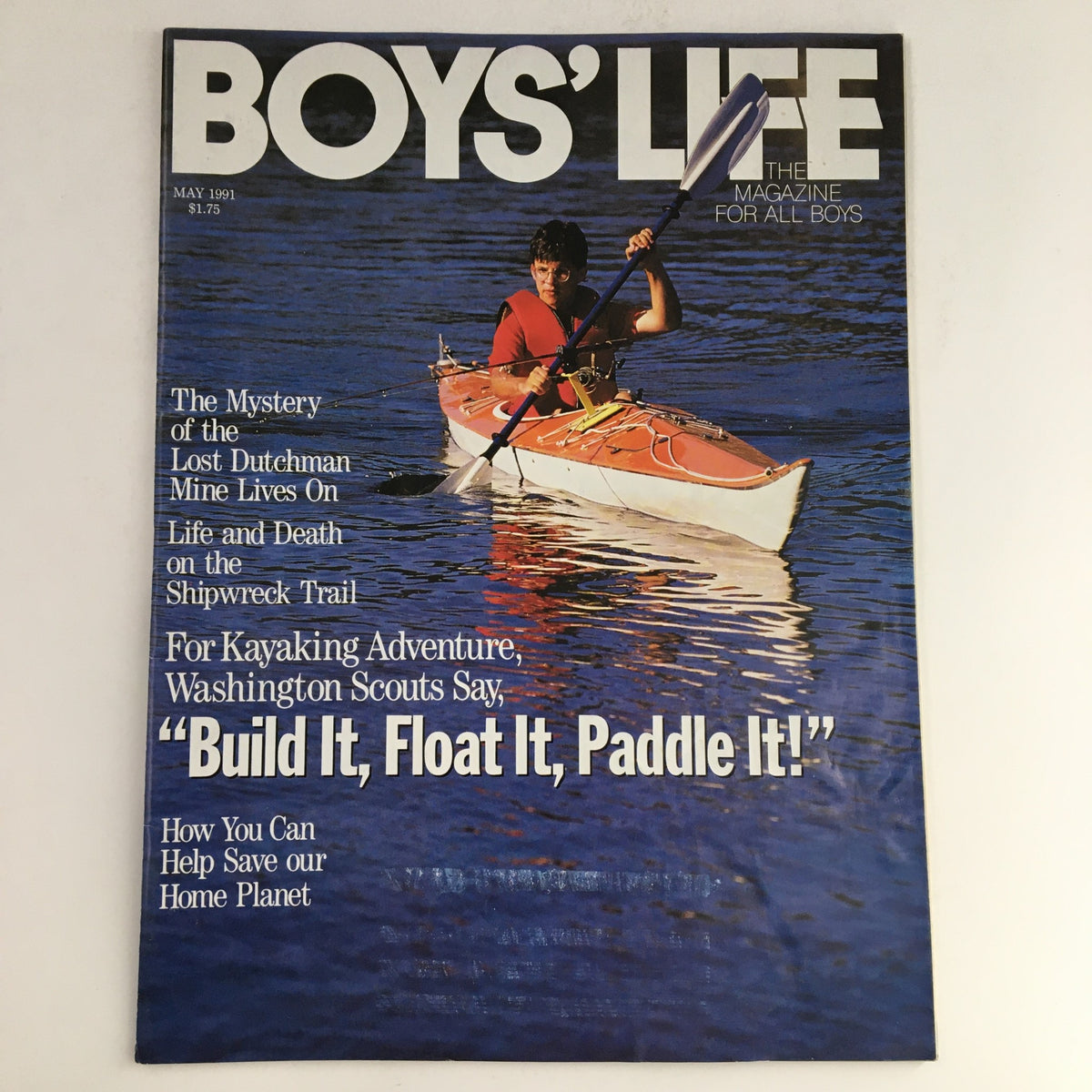 Boys' Life Magazine cover from May 1991 featuring the title 'The Mystery of the Lost Dutchman Lives On', showcasing a young boy kayaking in a bright orange kayak on a serene blue water background.