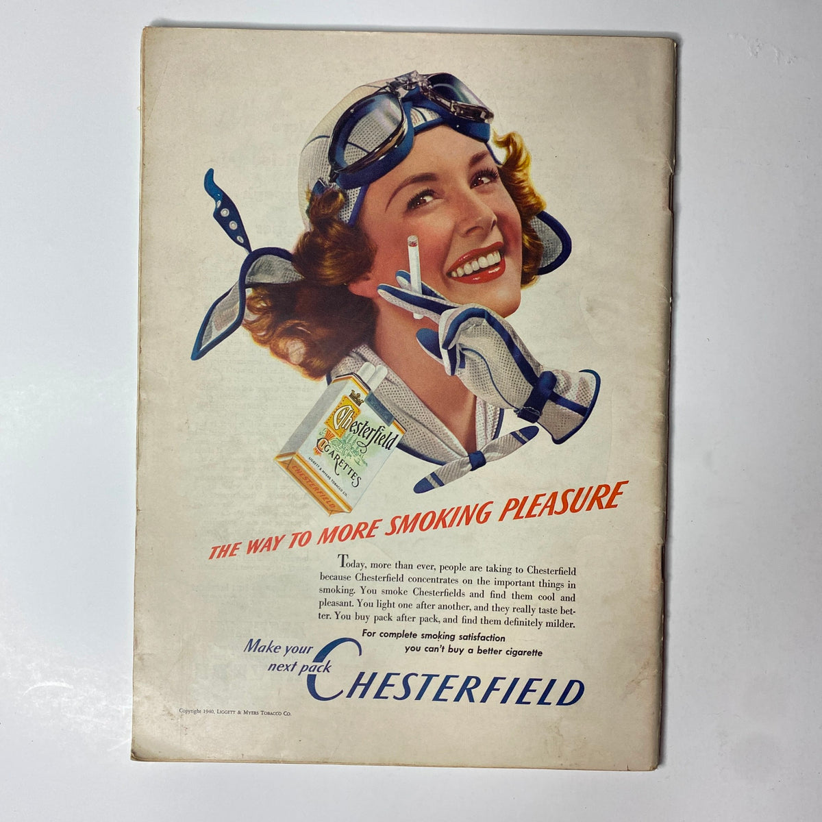 Vintage advertisement for Chesterfield cigarettes, depicting a smiling woman wearing an aviation helmet and gloves, promoting the slogan 'The Way to More Smoking Pleasure'.