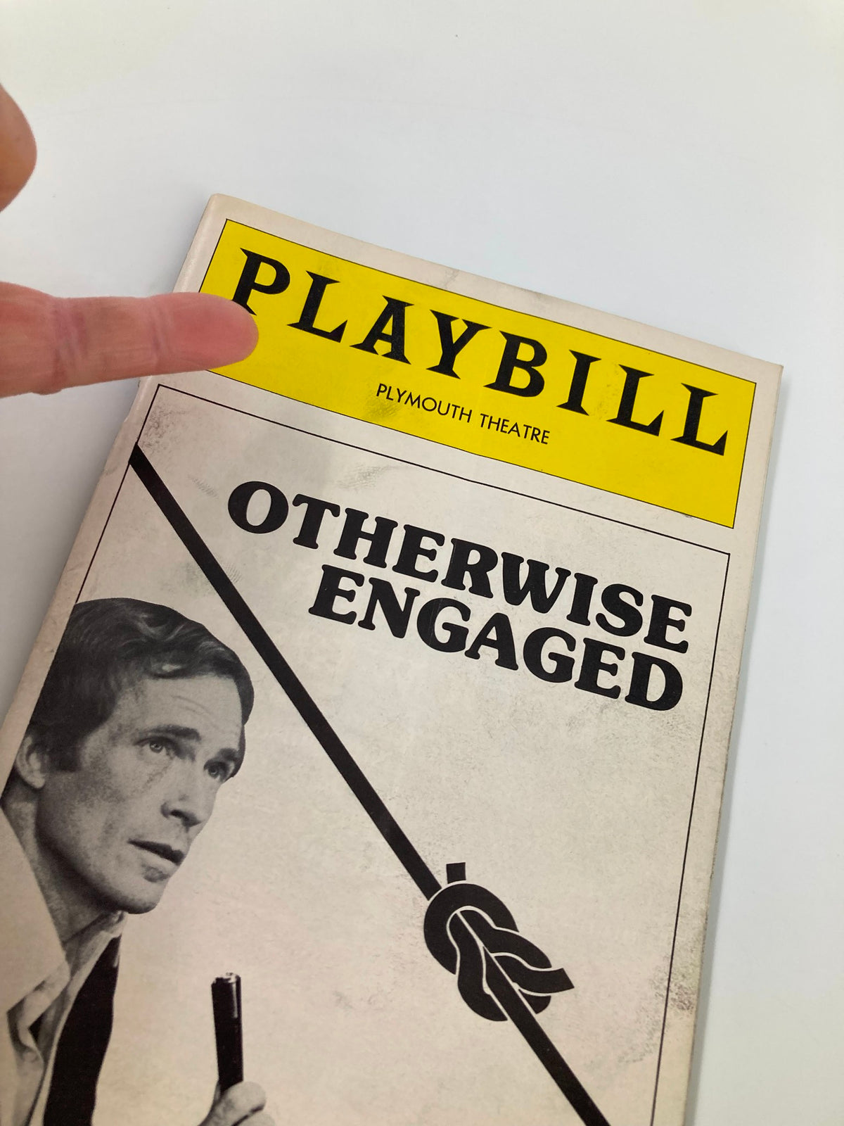 Close-up shot of the 1977 Playbill for 'Otherwise Engaged' at Plymouth Theatre showing the title and a finger pointing to it.