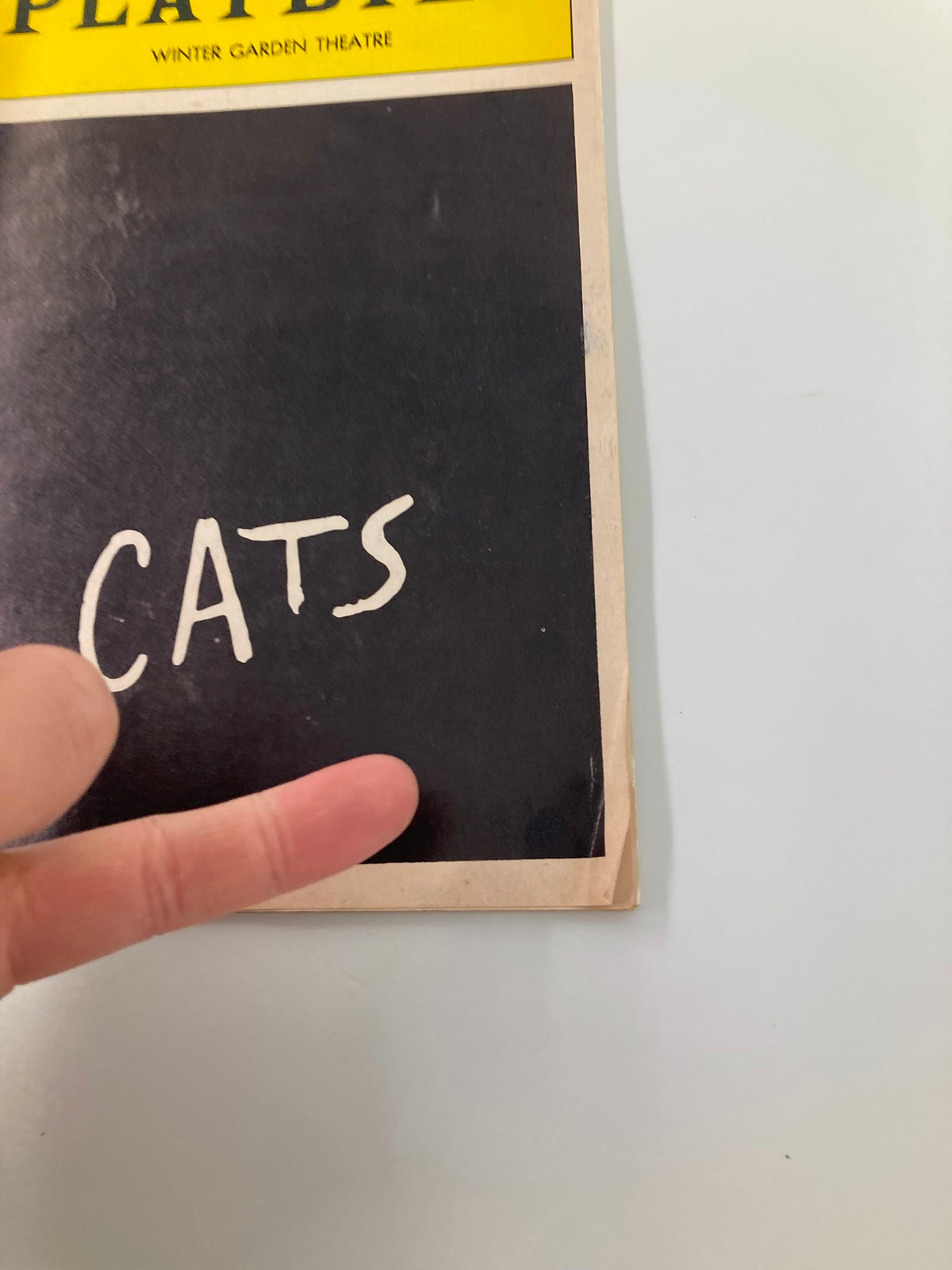 Close-up view of the 1992 Cats Playbill cover, displaying the title Cats with a finger pointing to the bottom right corner.