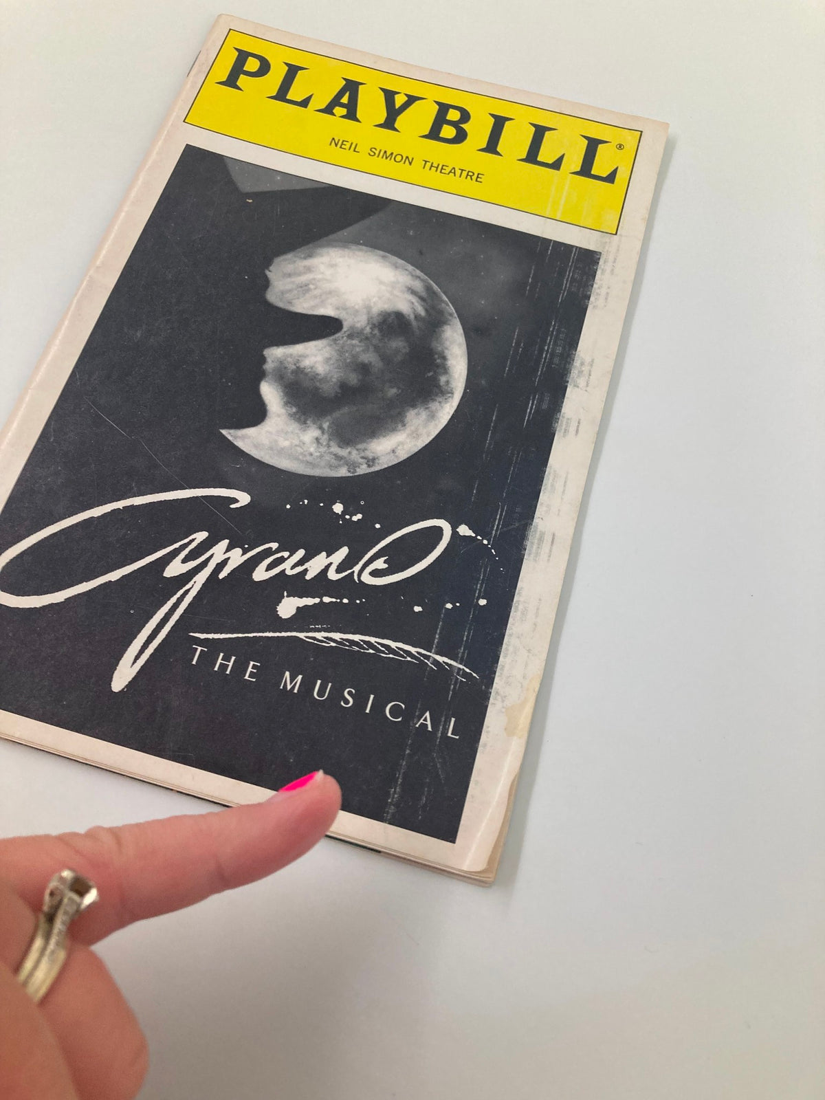 1994 Playbill for Cyrano the Musical at Neil Simon Theater displayed with a hand pointing to the cover, featuring moon and signature logo.