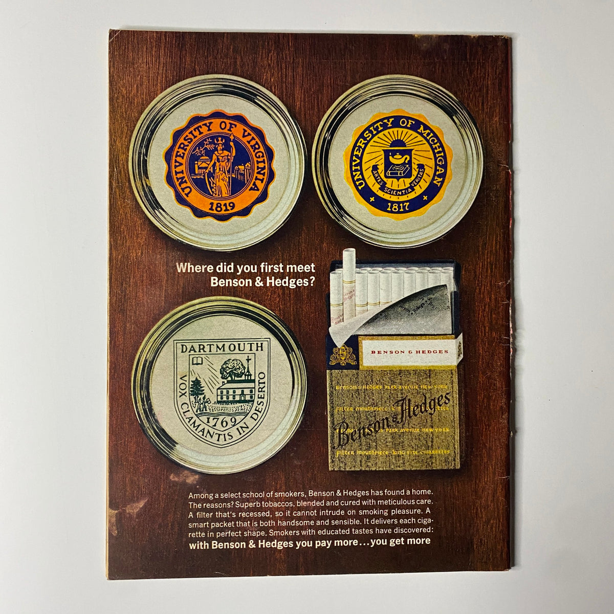 Retro advertisement for Benson & Hedges featuring a collection of academic seals from universities including the University of Virginia, University of Michigan, and Dartmouth, with the tagline 'Where did you first meet Benson & Hedges?'. This vintage design illustrates brand heritage and the appeal to educated smokers.