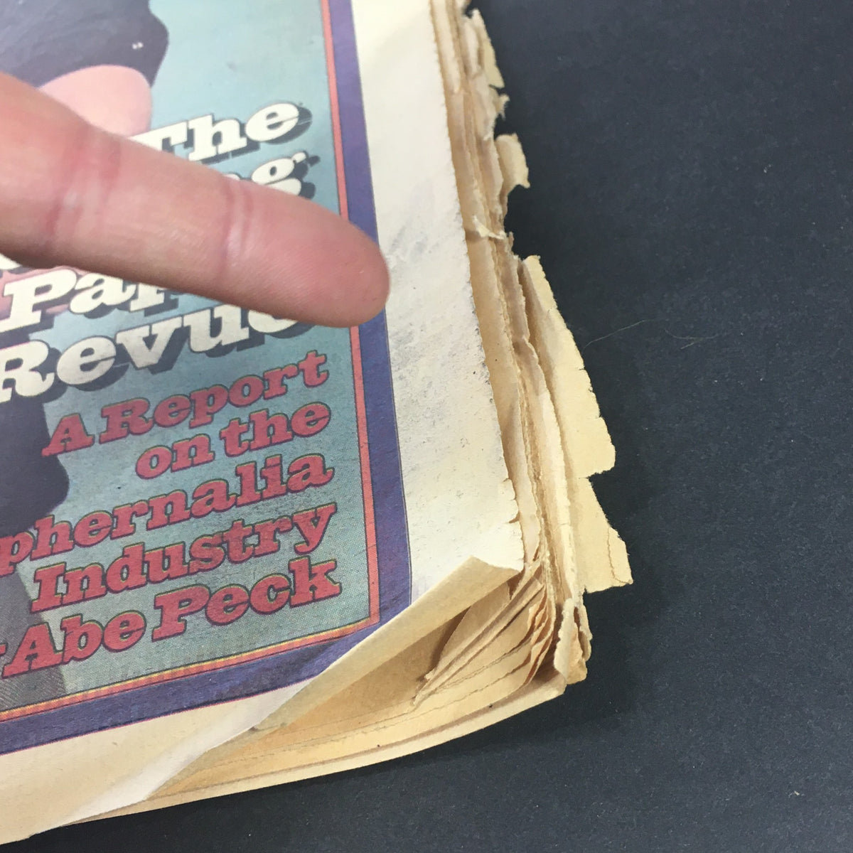 Side view of the VTG Rolling Stone Magazine January 27 1977 displaying the worn edges and layered pages, emphasizing its vintage condition with a finger pointing to the deterioration.