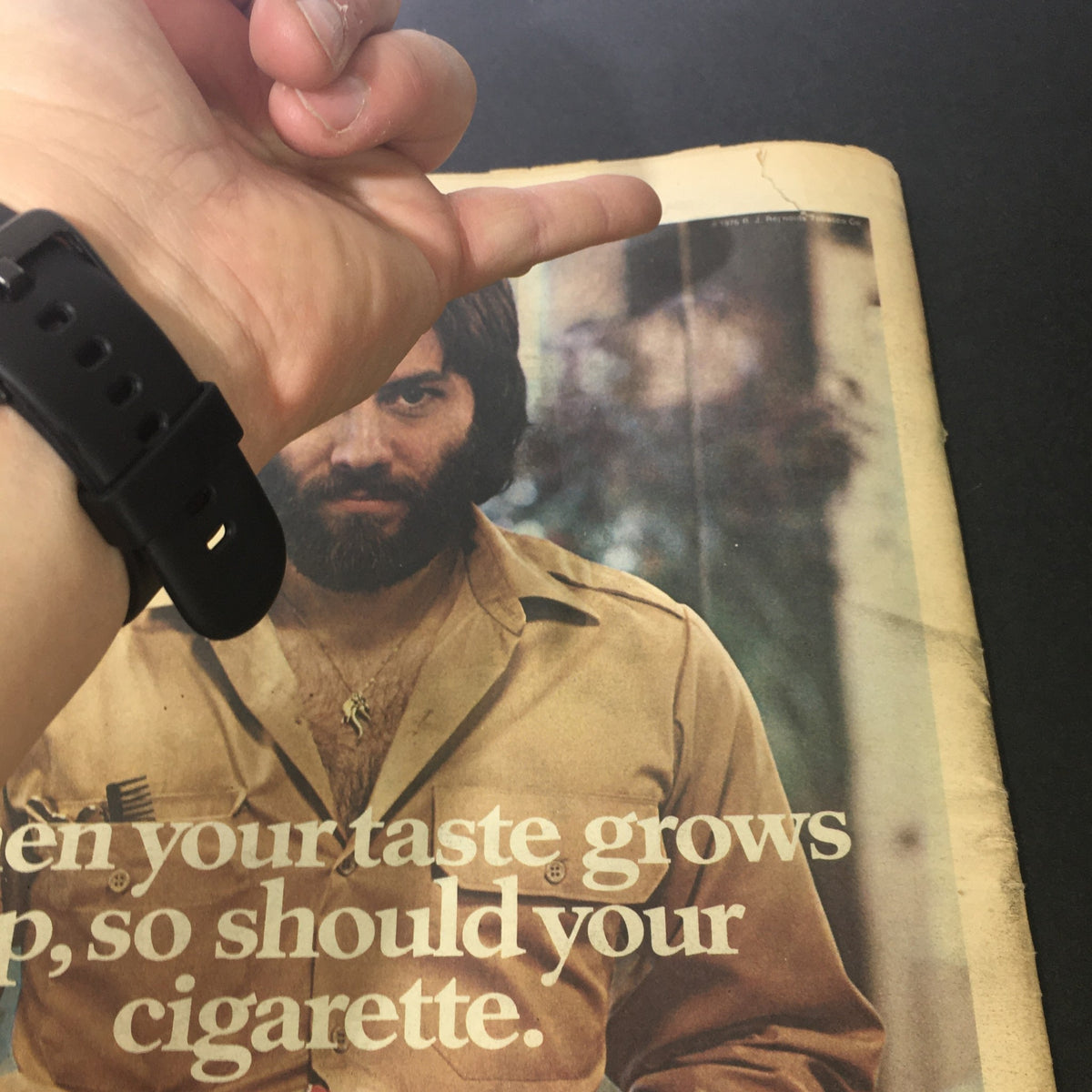 Interior view of the VTG Rolling Stone Magazine January 27 1977 showcasing a full-page advertisement with a person in a shirt, highlighting its age with visible wear and a finger pointing at a crease on the page.