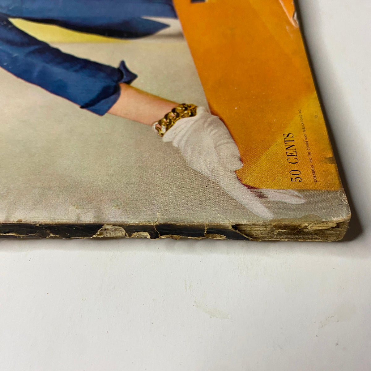 Close-up view of the bottom corner of Vogue Magazine May 1, 1955 Summer Fashion Textbook, showing minor wear and tear while displaying the artistic elements of mid-century fashion.