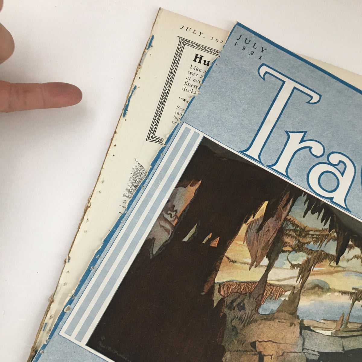 Detail showing the cover page of VTG Travel Magazine July 1921 with finger pointing towards the edge of the detached cover.