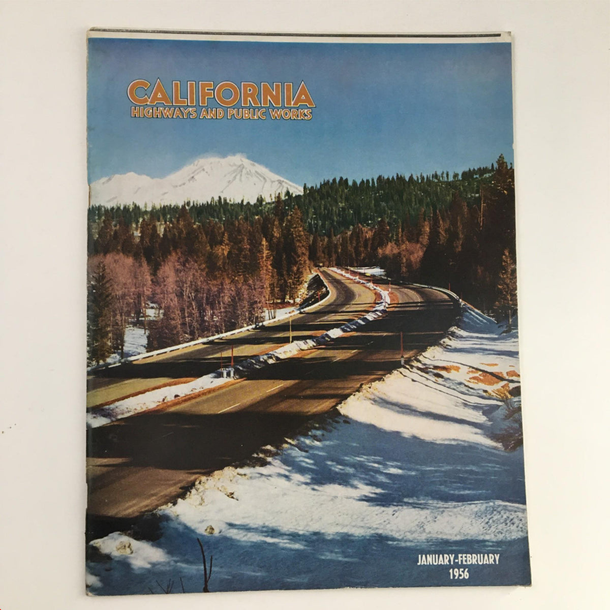 California Highway and Public Works January-February 1956 magazine cover showcasing a scenic highway surrounded by snow-capped mountains and pine trees.