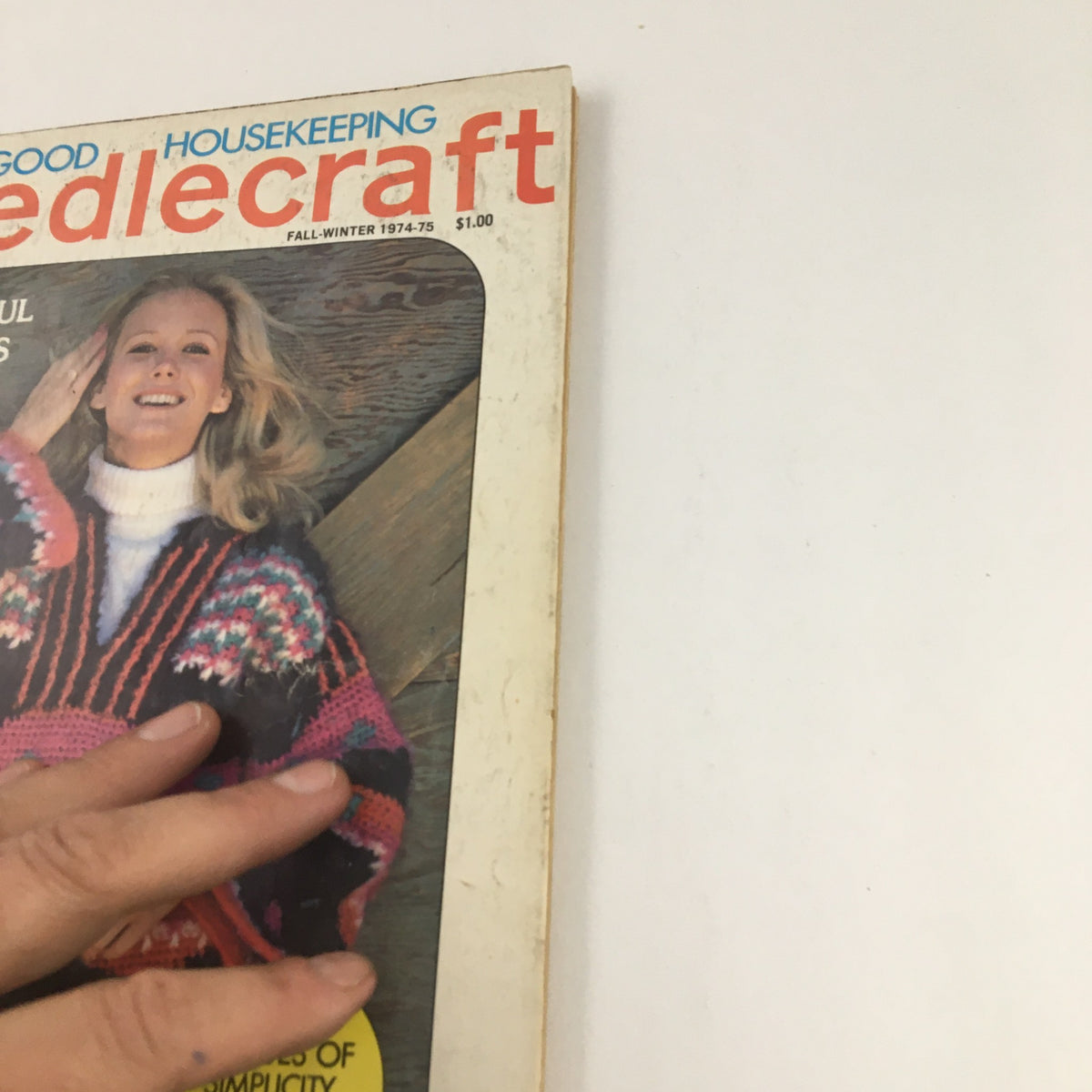 Close-up of the Good Housekeeping Needlecraft Fall 1974 cover, showcasing a woman in a vibrant sweater and the magazine's title and focus on beautiful new fashions.