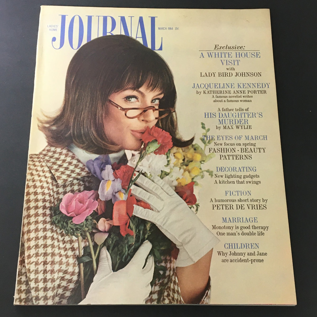 Cover of VTG Journal Magazine March 1964 featuring Jackie Kennedy and Lady Bird Johnson, showcasing a woman holding flowers with elegant fashion.