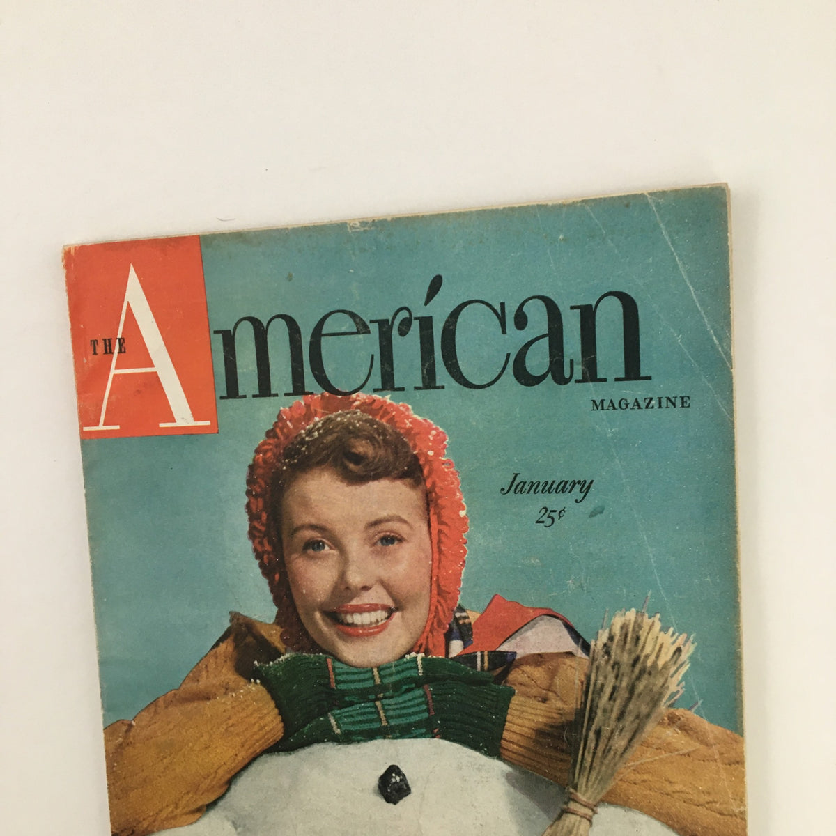 Close-up of the cover of The American Magazine January 1950, highlighting a joyful woman in winter attire beside a snowman, with mention of The Trial of Steven Kent.