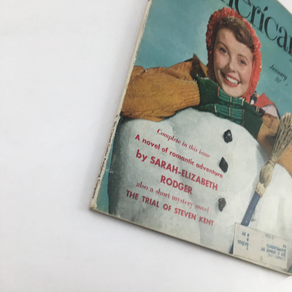 Detail view of The American Magazine January 1950 cover, featuring a cheerful woman in a winter hat and green gloves next to a snowman, promoting The Trial of Steven Kent.