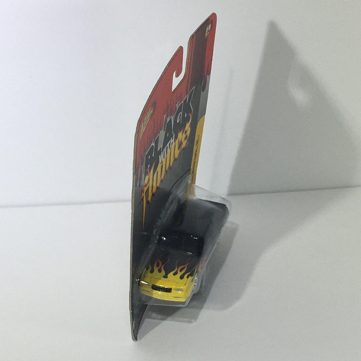 Side view of Johnny Lightning Black with Flames 1987 Chevy Monte Carlo SS die-cast car in its original packaging, highlighting its striking appearance.