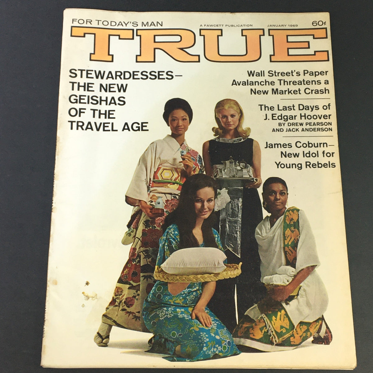 Cover of the January 1969 issue of True Magazine featuring the title 'VTG True Magazine January 1969 J. Edgar Hoover, Geishas of Travel Age, Newsstand'. The cover showcases diverse models dressed in colorful outfits representing Asian influences, with themes of travel and the portrayal of stewards as modern geishas. The magazine includes headlines about J. Edgar Hoover and cultural insights from the era.