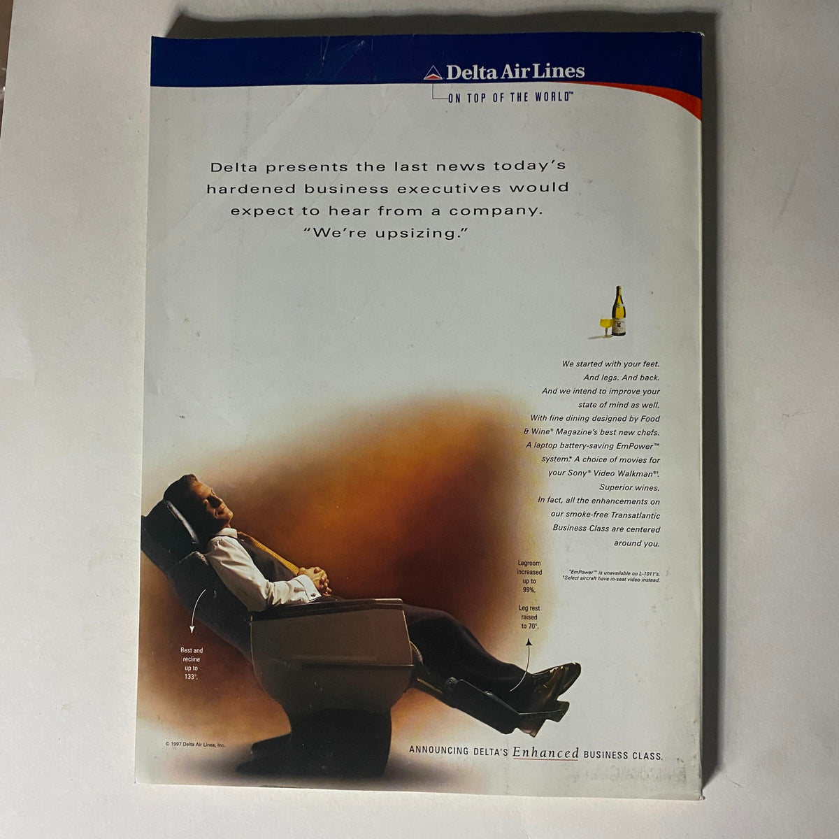 Promotional advertisement for Delta Air Lines showcasing the features of their Enhanced Business Class service. The image features a relaxed business executive reclining in a comfortable seat, highlighting the luxurious experience and commitment to service. The text includes the tagline 'We're upsizing' and mentions improvements to in-flight comfort.