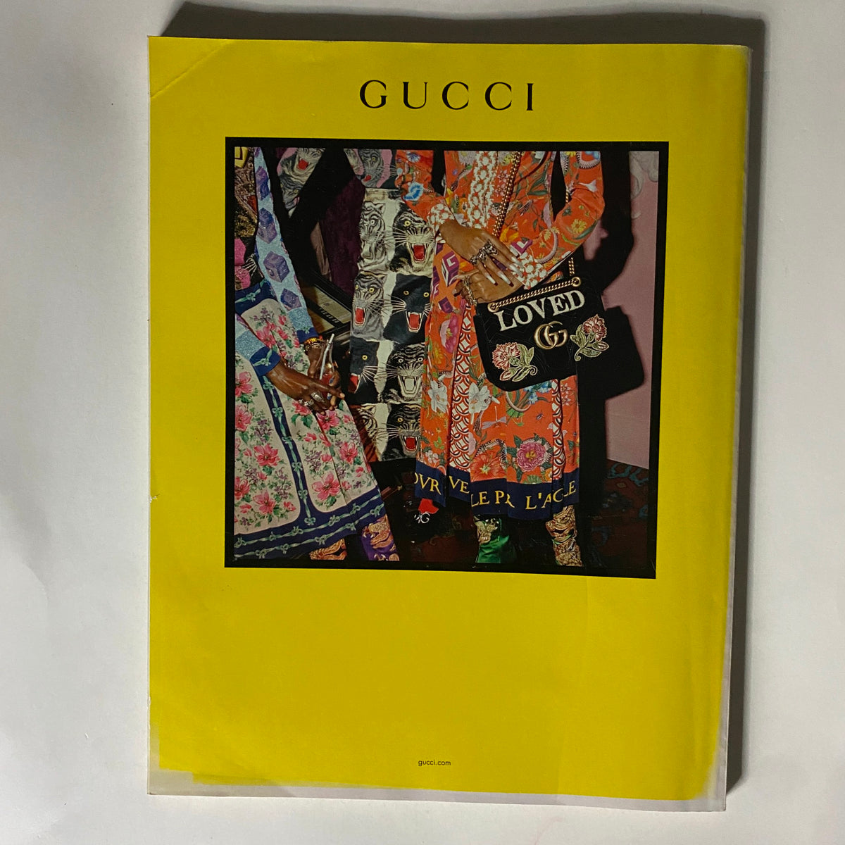 Cover of a Gucci fashion catalog in vibrant yellow featuring a creative display of patterned clothing and detailed accessories, showcasing bold fashion statements.