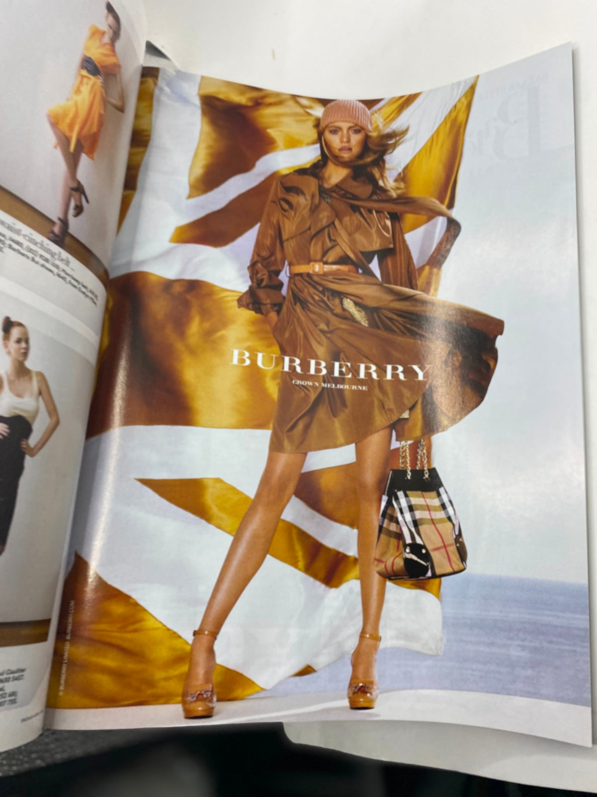 Burberry fashion advertisement featured in Harper's Bazaar Australia Magazine 2018, showcasing a model in a stylish brown trench coat with a bold background, promoting high-fashion clothing and accessories.