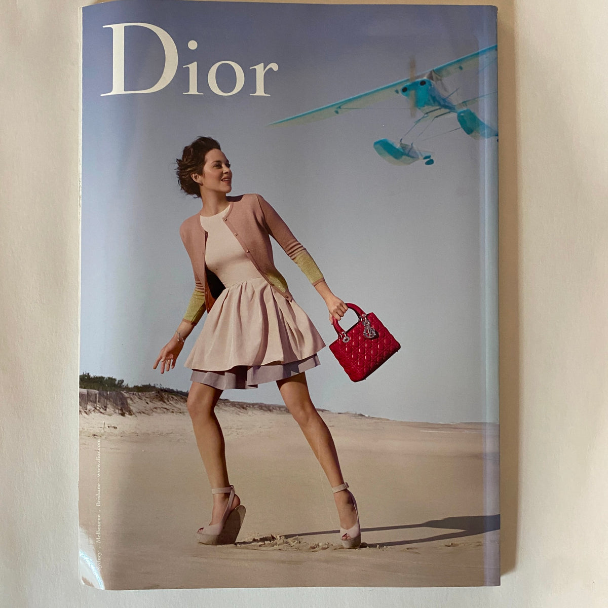 Harper's Bazaar Australia Magazine December 2012 featuring a fashion model in a chic pink dress with a stylish handbag, set on a beach with an airplane in the background.