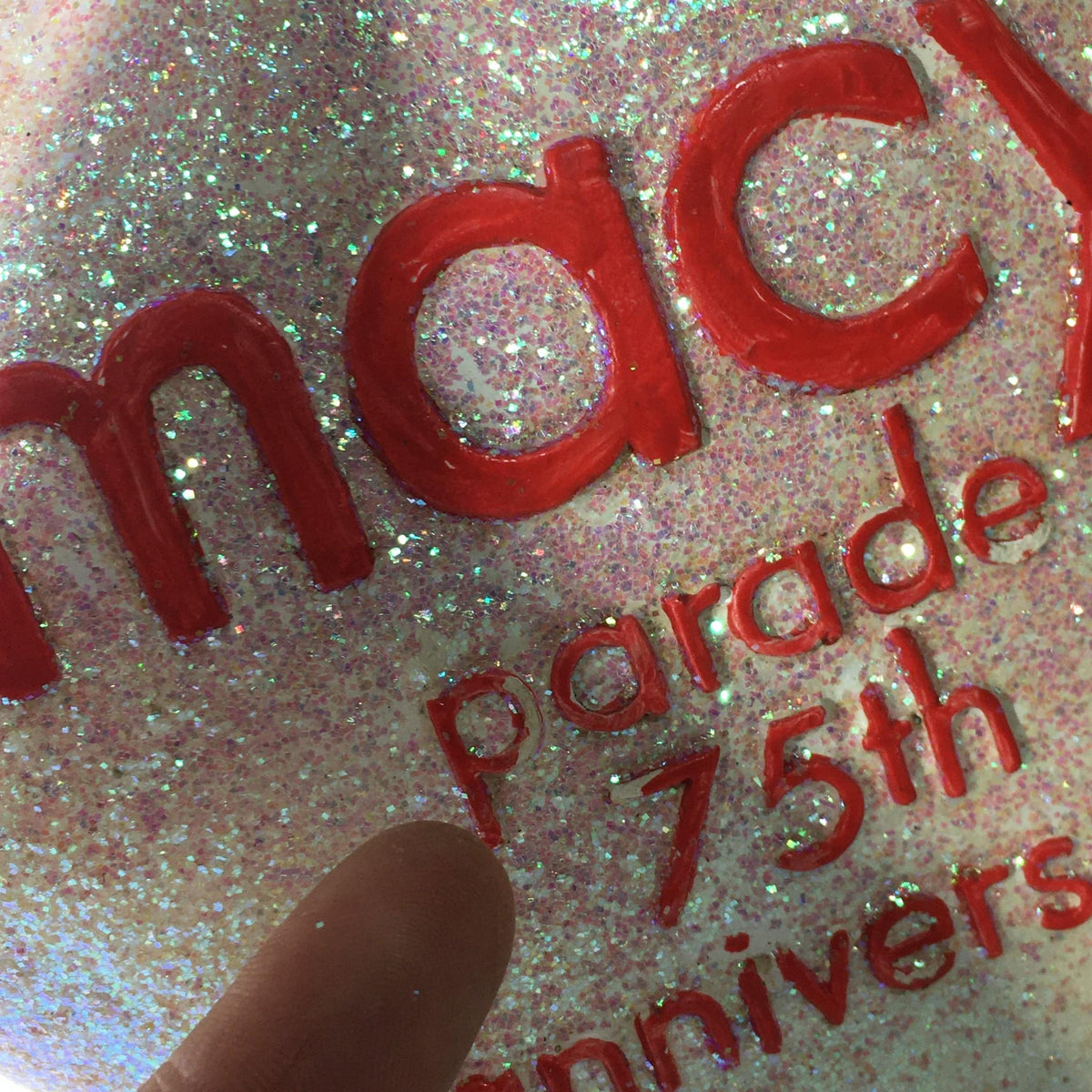 Close-up of the glittery surface of the Macy's Thanksgiving Day Parade 75th Anniversary Collectible star ornament, highlighting the text 'parade 75th anniversary'.